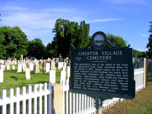 Sign at Chester Village Cemetery, detailing its history and notable figures, surrounded by gravestones and greenery.