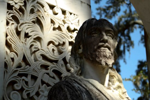 A close-up of a weathered statue of a bearded figure against an ornate stone background.