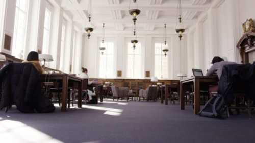 A spacious library with tall windows, featuring study tables and students working quietly.