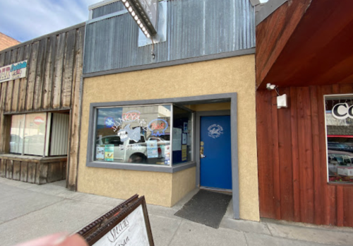 A storefront with a blue door and a sign, featuring a wooden facade and nearby signage in a small town.