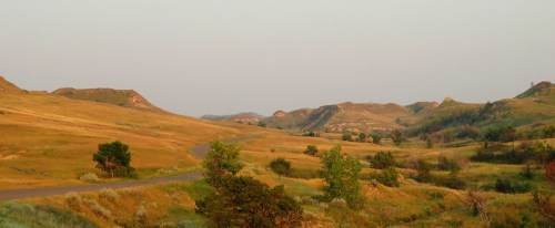 A serene landscape featuring rolling hills, grassy plains, and a winding road under a soft, hazy sky.