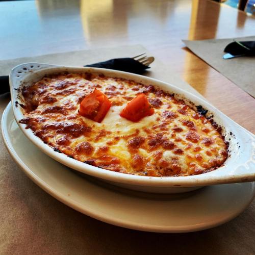 A baked dish with melted cheese and two pieces of orange carrot on top, served in a white oval dish.
