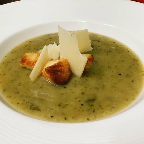 A bowl of green soup topped with croutons and cheese, served in a white dish.