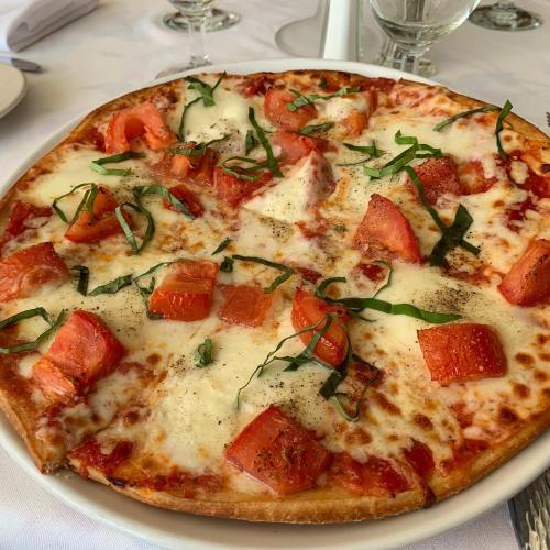 A freshly baked pizza topped with tomatoes, mozzarella cheese, and fresh basil on a white tablecloth.