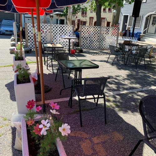 Outdoor dining area with tables, chairs, and flower planters, shaded by red and blue umbrellas.