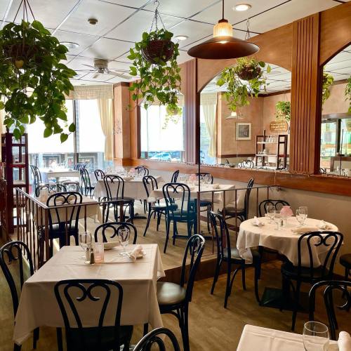 A cozy restaurant interior with tables set for dining, surrounded by hanging plants and warm lighting.