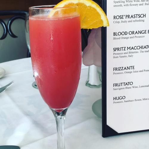 A refreshing pink cocktail garnished with an orange slice, next to a menu on a table.