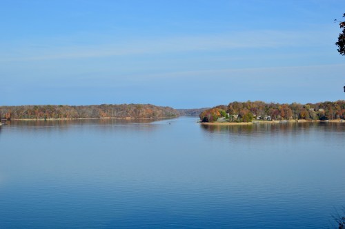 A serene lake surrounded by autumn-colored trees under a clear blue sky.