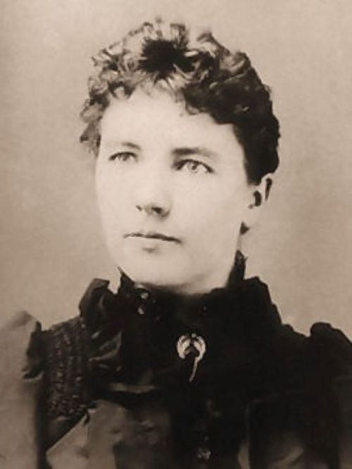 Black and white portrait of a woman with curly hair, wearing a dark dress with a high collar and a brooch.
