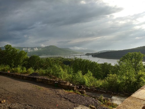A scenic view of a river winding through green hills under a cloudy sky, with a bridge in the distance.