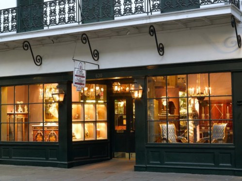 A charming antique shop with large windows displaying elegant furniture and decor, set in a historic building.