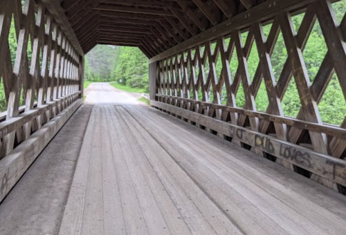 Interior view of a wooden covered bridge, featuring a diamond-patterned design and a clear path leading out.