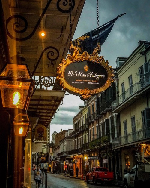 A vintage shop sign for M.S. Rau Antiques hangs above a rainy street lined with historic buildings.