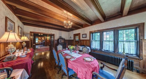 A cozy dining room with a wooden ceiling, elegant table settings, and large windows, featuring warm lighting and decor.