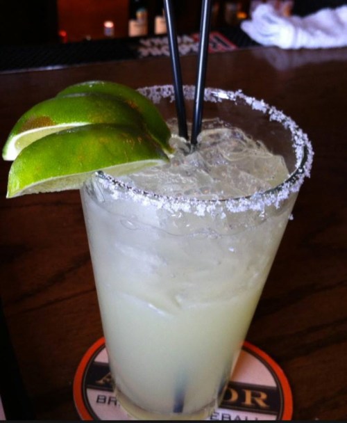 A refreshing margarita with lime wedges and salt on the rim, served with two straws.