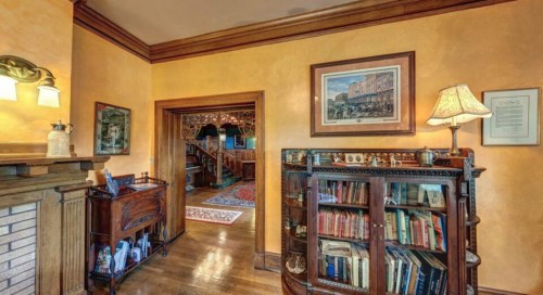 Cozy interior featuring a wooden bookshelf, warm lighting, and a view into a hallway with decorative art.