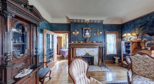 A vintage living room featuring ornate furniture, a marble fireplace, and blue wallpaper with decorative accents.