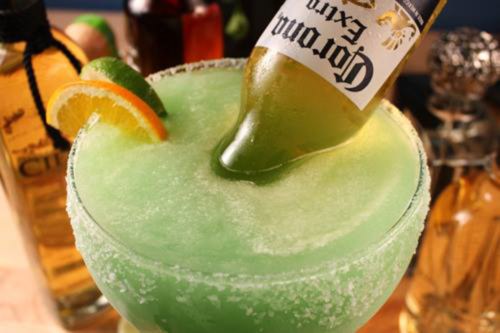 A vibrant green margarita with a beer bottle resting in it, garnished with lime and orange slices.