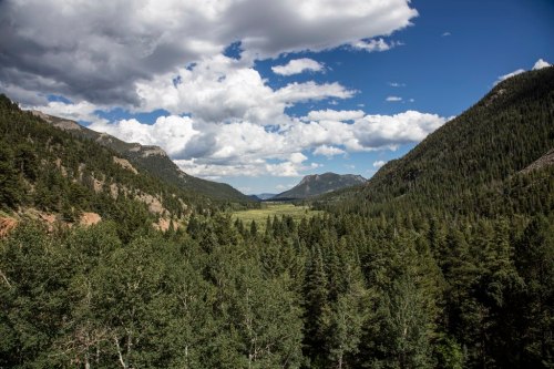 A scenic view of a lush green valley surrounded by mountains under a partly cloudy sky.