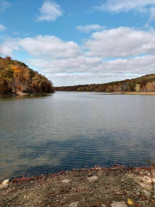 A serene lake surrounded by autumn foliage under a partly cloudy sky.
