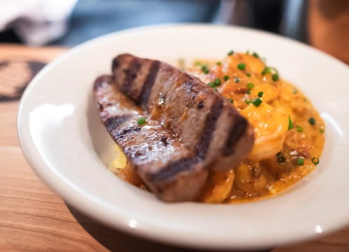 A plate of creamy shrimp and grits topped with grilled sausage and garnished with chopped chives.