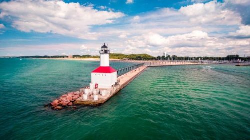 A lighthouse on a pier extends into turquoise waters under a partly cloudy sky.