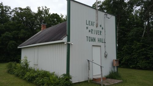 A small, white building with "Leaf River Town Hall" painted on the side, surrounded by greenery.