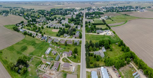 Aerial view of a rural town with residential areas, fields, and a main road running through the landscape.