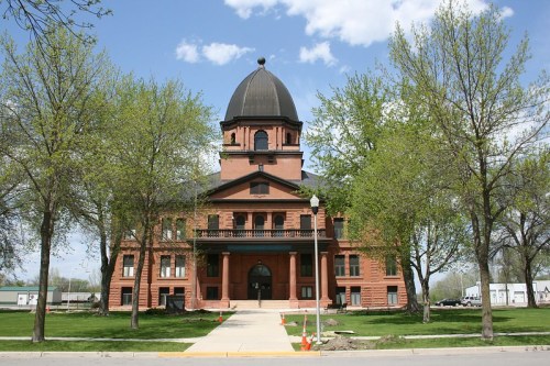 Historic brick building with a dome, surrounded by trees and a clear blue sky. Pathway leads to the entrance.