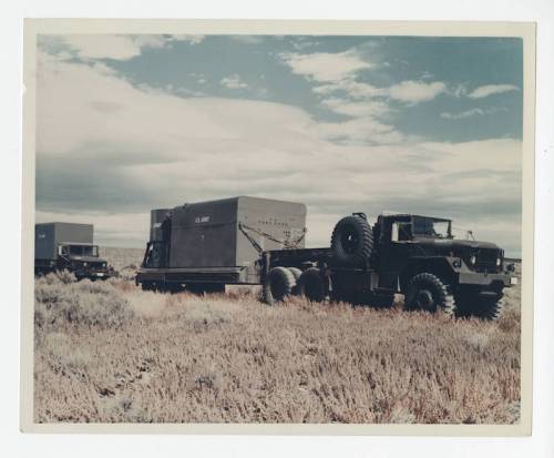 Military trucks parked in a desert landscape, with a large cargo container labeled "U.S. Army" nearby.