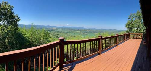 A panoramic view from a wooden deck overlooking lush green hills and mountains under a clear blue sky.