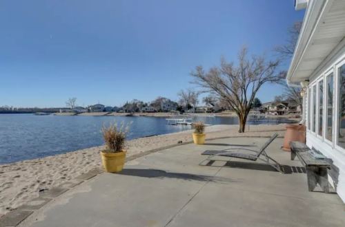 A serene lakeside view with sandy shore, potted plants, and a clear blue sky.
