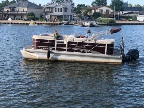 A pontoon boat with two people enjoying a day on the water, surrounded by houses and greenery.