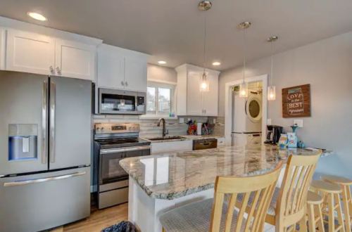 Modern kitchen with white cabinets, stainless steel appliances, a large granite island, and wooden bar stools.