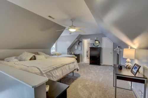 Cozy attic bedroom with two beds, a ceiling fan, and soft lighting, featuring a dresser and a small desk.