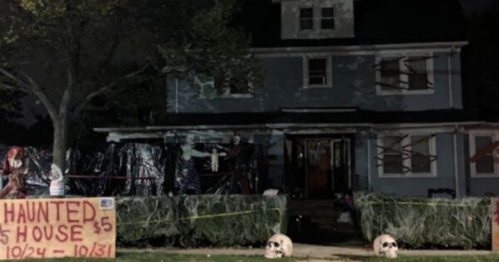 A spooky house decorated for Halloween with skeletons, cobwebs, and a sign for a haunted house event.