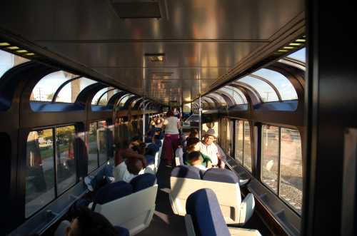 Interior of a train car with passengers seated, large windows allowing natural light to fill the space.