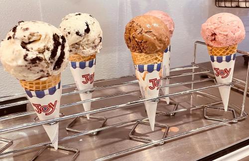 Five ice cream cones with various flavors, including chocolate, strawberry, and cookies and cream, displayed on a rack.