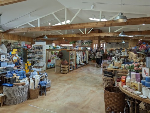 A cozy store interior filled with various home goods, plants, and decorative items, with shoppers browsing the aisles.