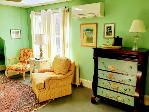 Cozy room with green walls, a patterned chair, a dresser, and natural light from a window.