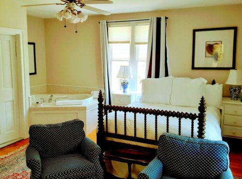 Cozy bedroom featuring a bed, two chairs, a lamp, and a jacuzzi tub in a warm, inviting setting.