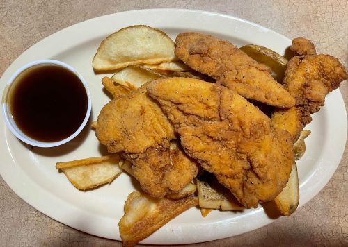 A plate of fried chicken tenders with golden-brown potato wedges and a small cup of dipping sauce.
