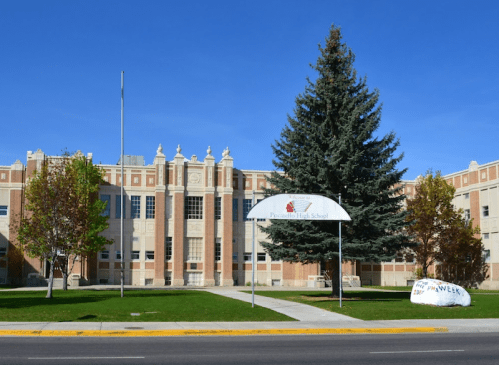 Exterior view of Pasco High School, featuring a large tree, grassy area, and a sign for homecoming week.