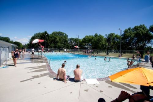 A sunny day at a public pool with people swimming, lounging, and enjoying the water under clear blue skies.