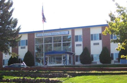 Exterior view of Power County Hospital District building with flag, trees, and a grassy area in front.