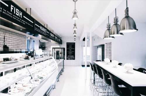 A modern seafood market with a bright interior, featuring a display case and sleek black seating.