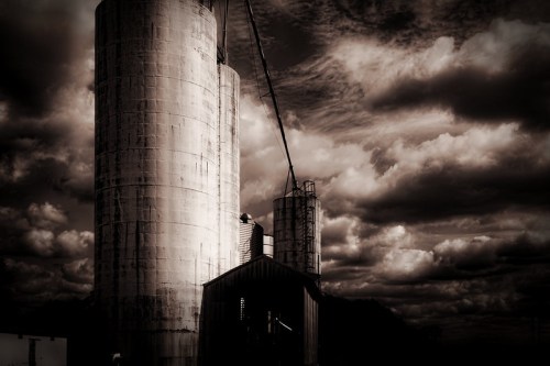 Black and white image of tall silos against a dramatic, cloudy sky.