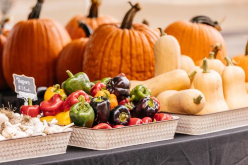 A display of pumpkins and colorful peppers, with squash and garlic, at a farmers' market.