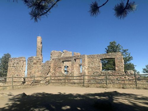 Ruins of a stone building surrounded by trees and a wooden fence under a clear blue sky.