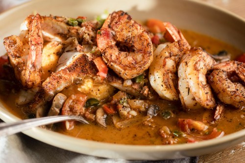 A close-up of a flavorful shrimp dish with spices, tomatoes, and vegetables in a creamy sauce, served in a bowl.